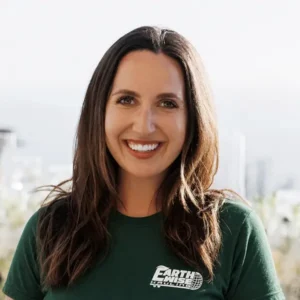 Smiling woman with long dark hair wearing a green EarthWise shirt, with a city skyline in the background.