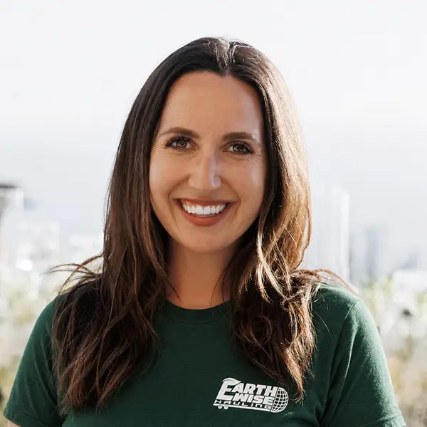 Smiling woman with long dark hair wearing a green EarthWise shirt, with a city skyline in the background.